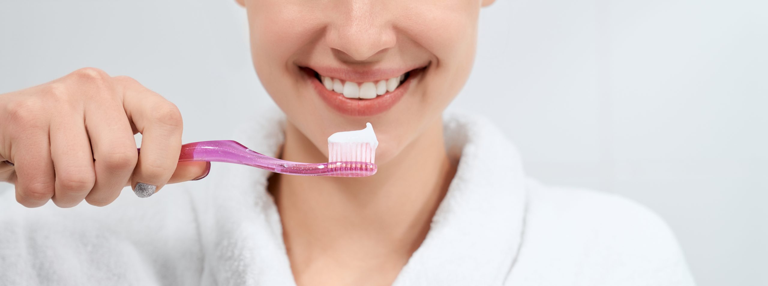 Woman in white robe holding toothbrush with paste.